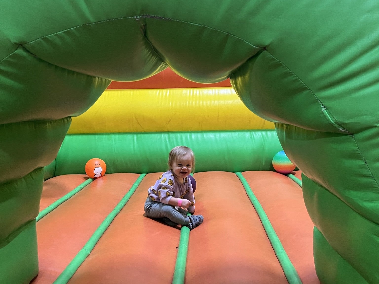 Toddler sitting under the green arch of an inflatable structure smiling